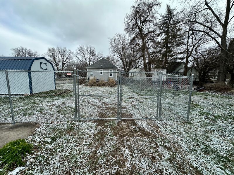 Snow-dusted fenced garden beds in a backyard with bare trees and a blue shed.