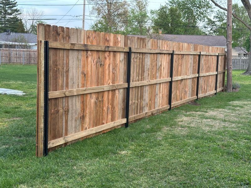 Weathered wooden privacy fence with posts, seen along a grassy backyard edge