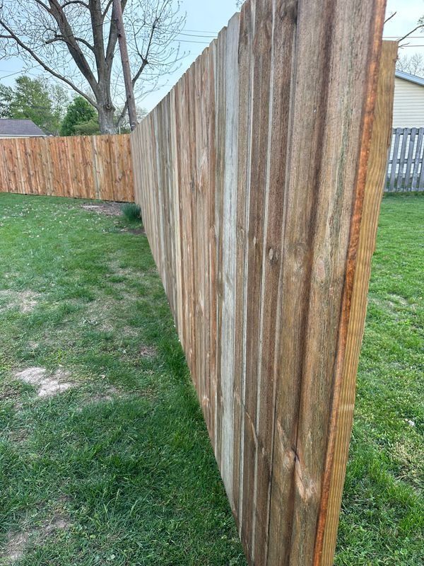 Weathered wooden fence along a grassy backyard, with a tree and neighboring houses in the background