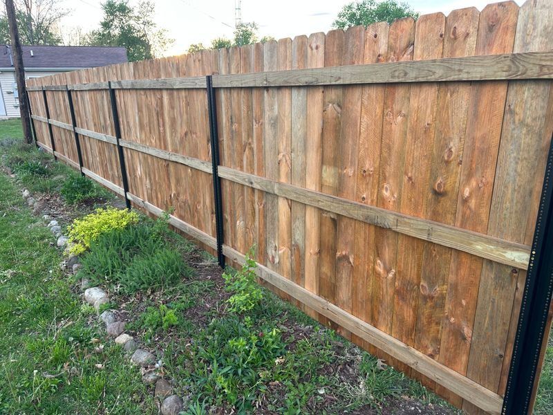 Wooden backyard fence with black metal posts beside a grassy strip and stone border