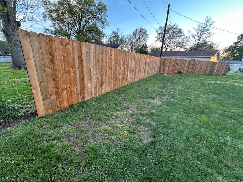 Long wooden privacy fence along a grassy yard at sunset, with trees and utility lines in the background