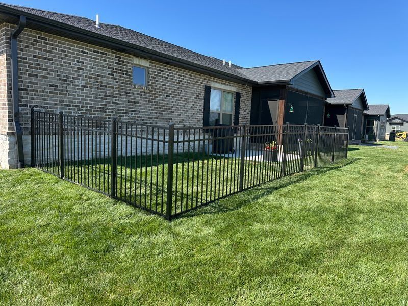 Brick apartment building with black metal fence enclosing a small grassy yard in bright sunlight