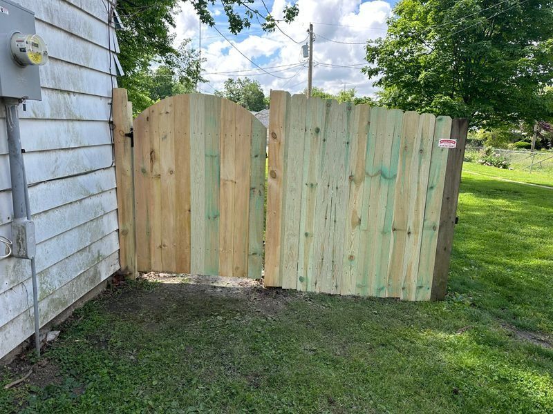 Wooden gate panels attached to a house, standing at the edge of a grassy yard.