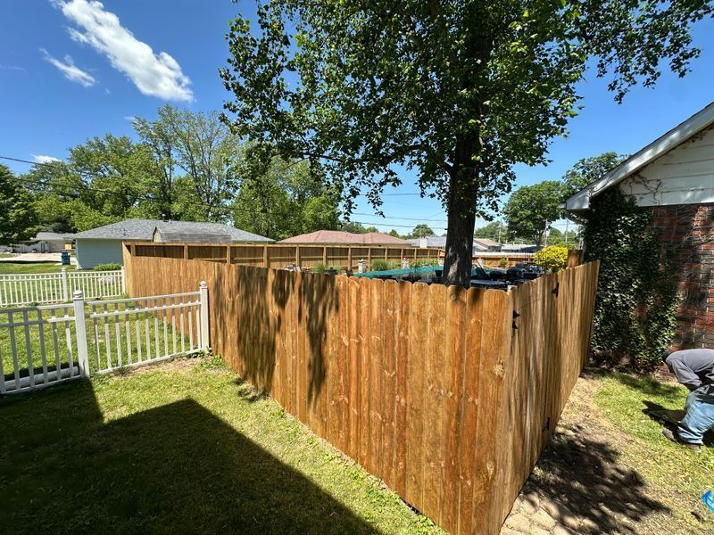 Wooden privacy fence under construction in a sunny backyard, with a person working at the right edge.
