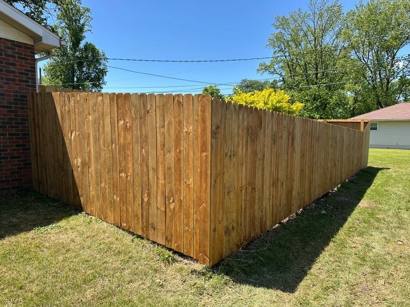 Wooden privacy fence enclosing a backyard, with a brick house and trees in the background.