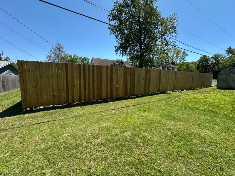 Wooden privacy fence along a grassy backyard under a clear blue sky
