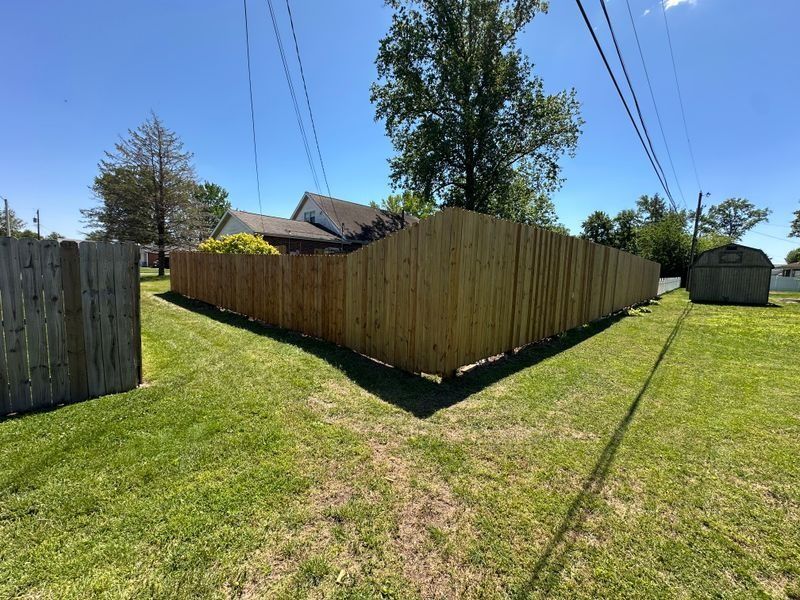 Backyard with a wooden privacy fence, green grass, trees, and a bright blue sky