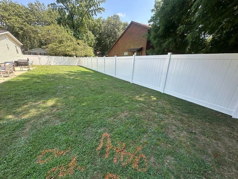 Sunny backyard with green lawn, white fence, and a small house in the background