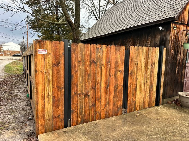 Wooden privacy fence with vertical planks beside a shed and muddy driveway