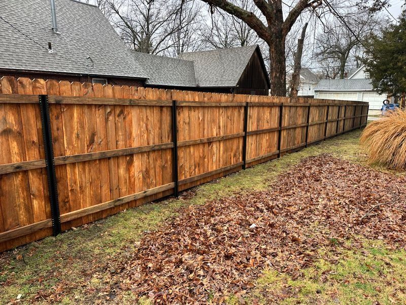 Wooden privacy fence beside a leaf-covered yard with trees and houses in the background.