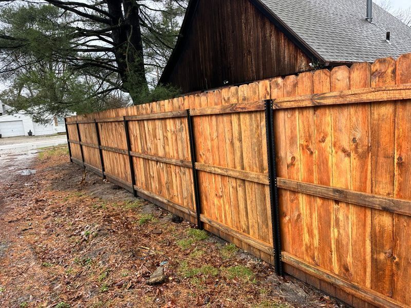 Wooden privacy fence beside a wet driveway and house on a rainy day