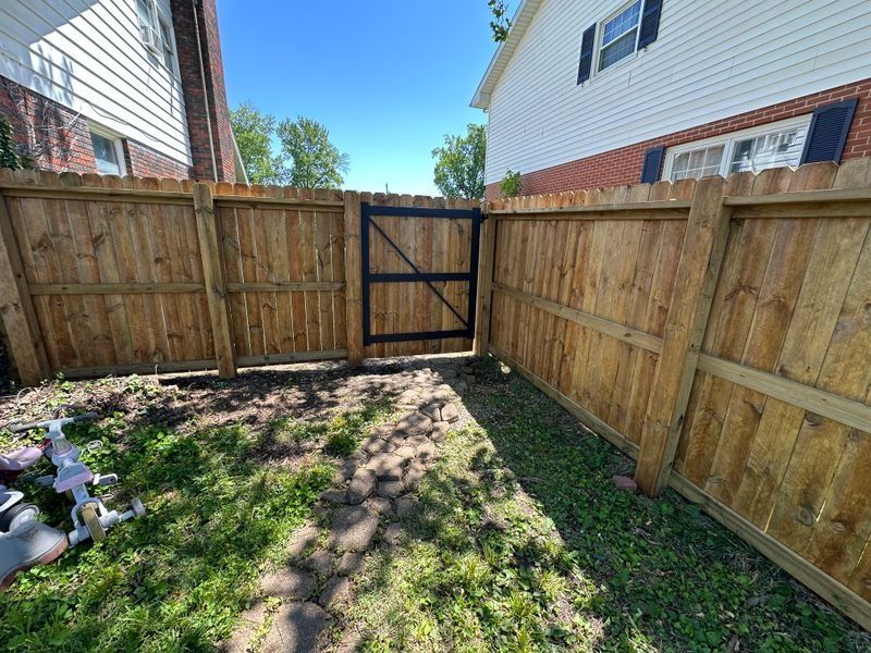Backyard with wooden fence and gate, patchy grass, and neighboring houses on both sides