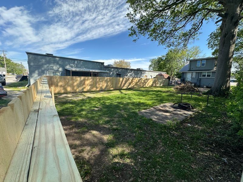 Backyard with wooden fence, grassy yard, and blue sky beside a house and apartment building