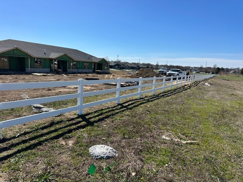 White fence along grassy field beside suburban homes under a clear blue sky