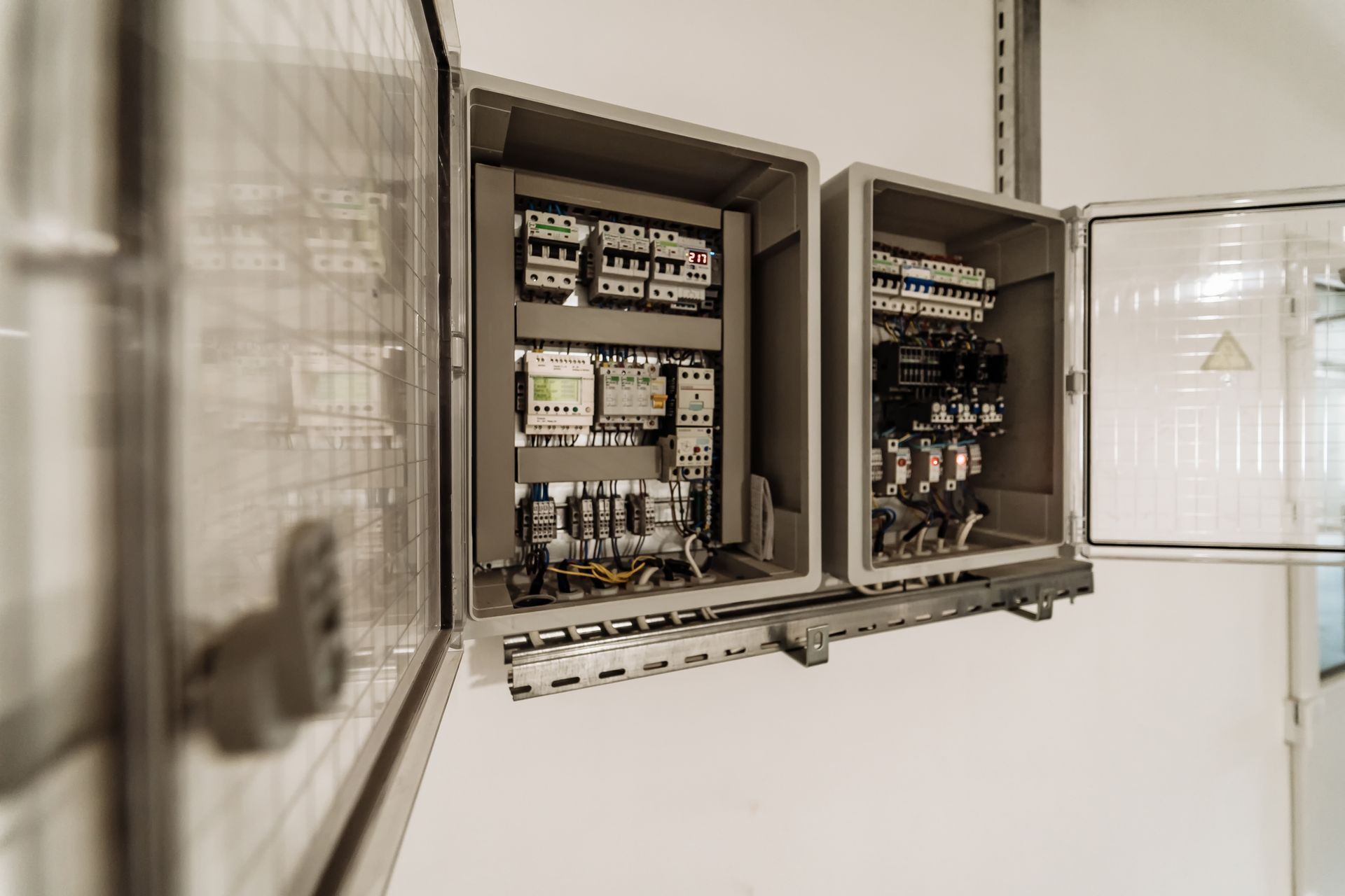 Two open electrical control panels mounted on a white wall, filled with wiring and components.