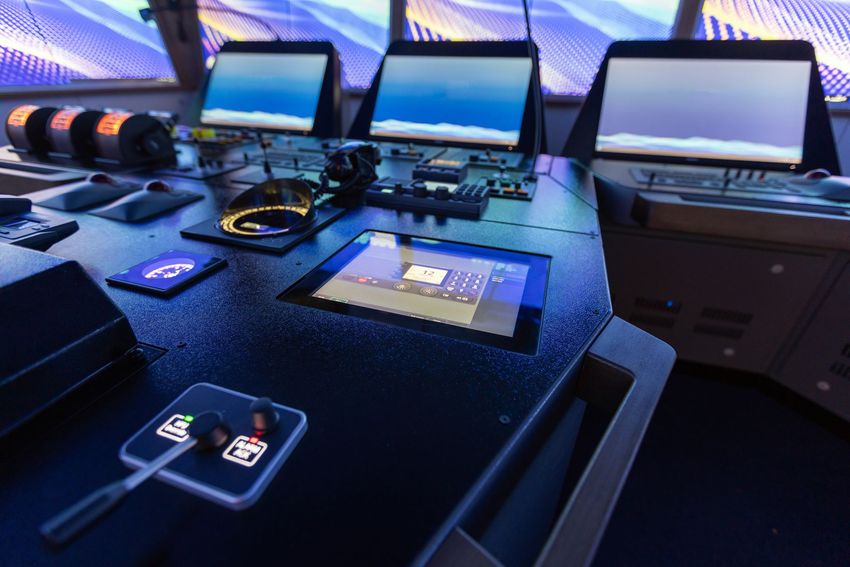 Cockpit console with three computer screens and control panels, illuminated blue.
