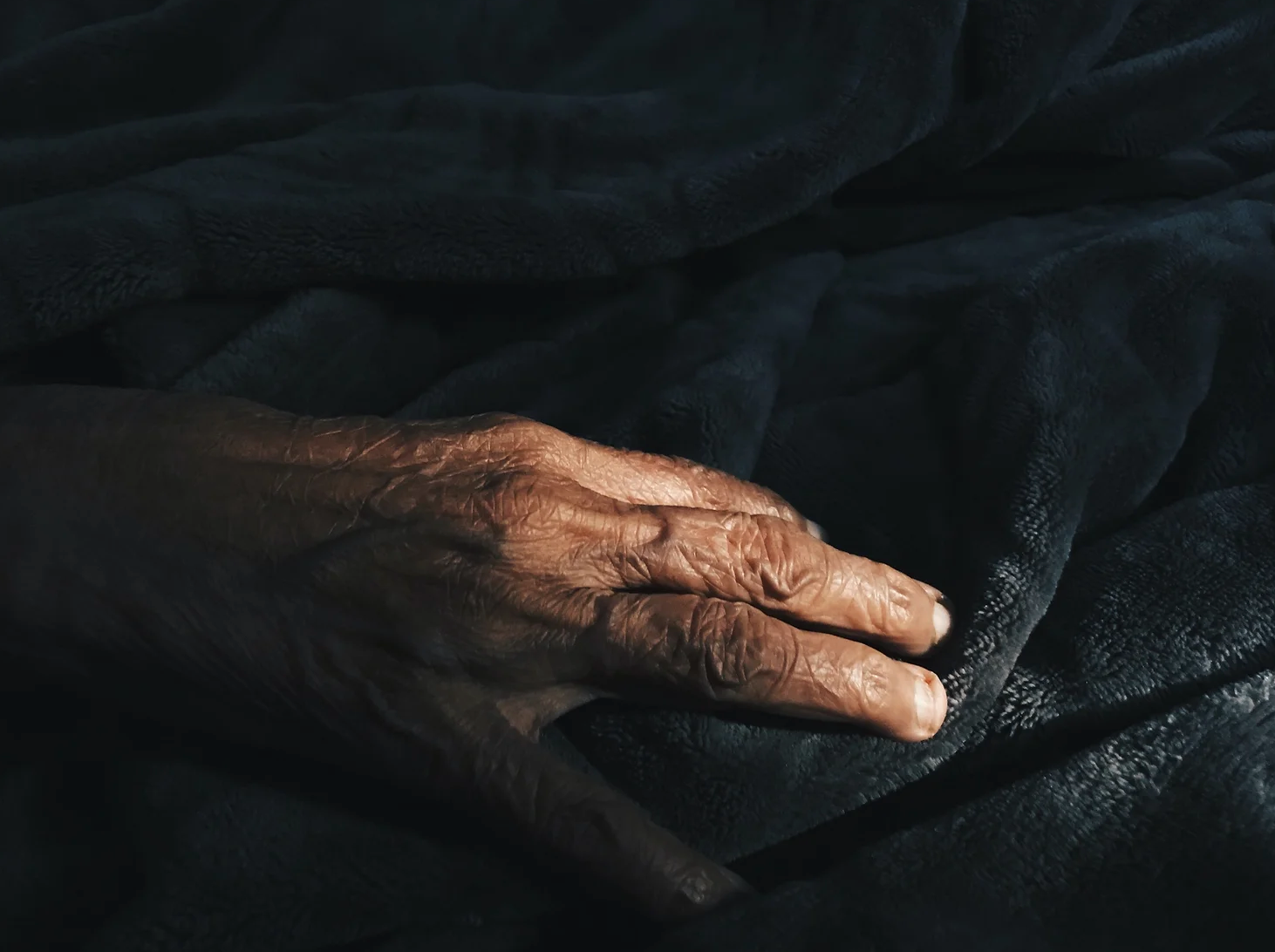 An elderly woman 's hand is laying on a black blanket.