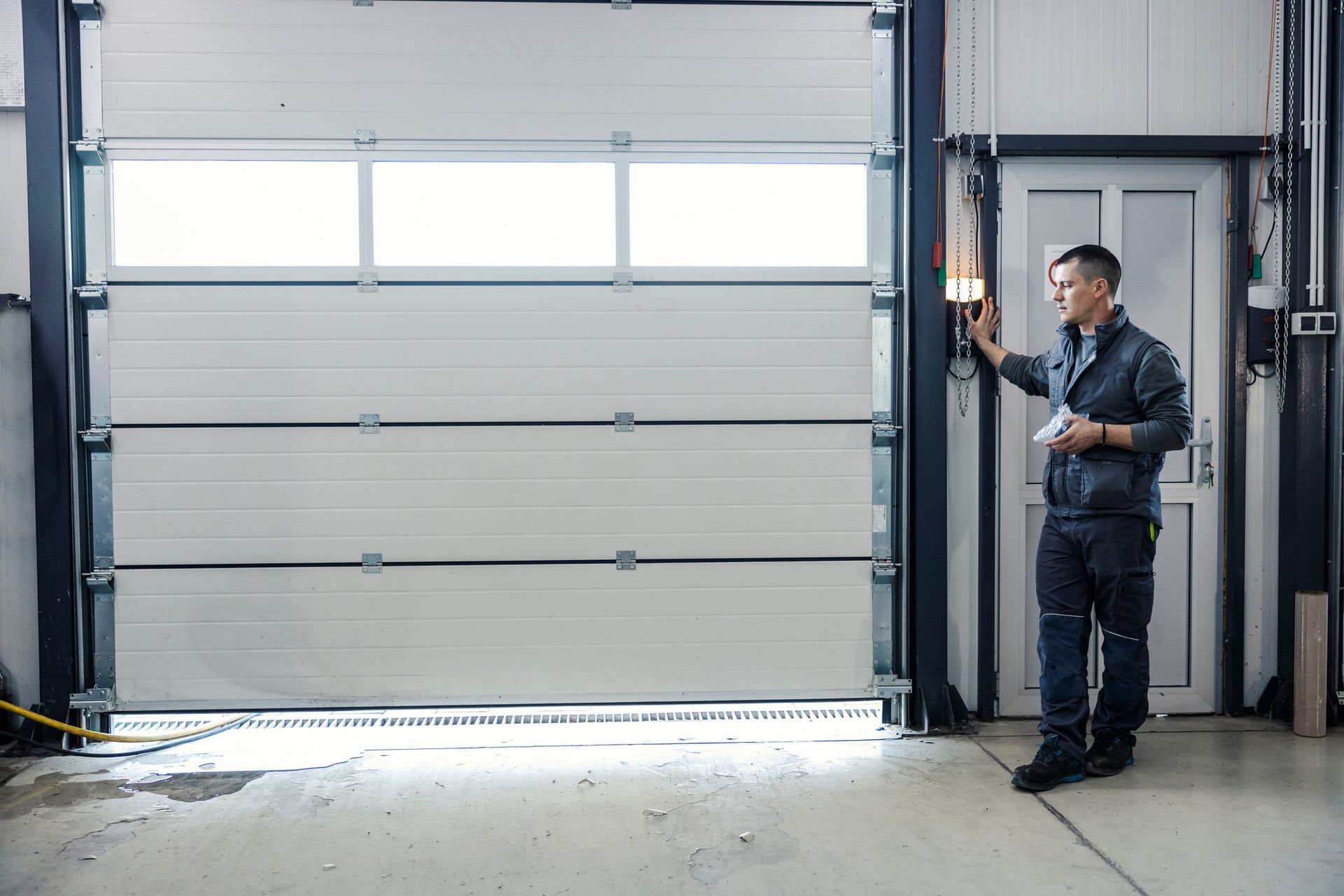 Man in work clothes operating a large white garage door in a warehouse.