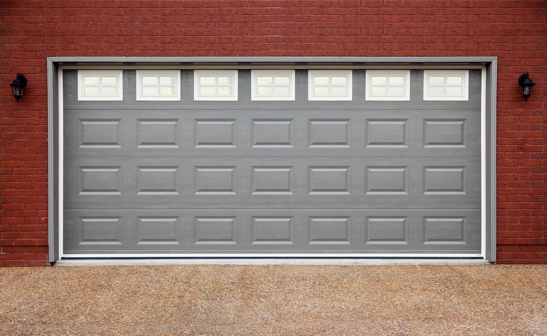 Gray garage door with upper window panels, brick wall backdrop.