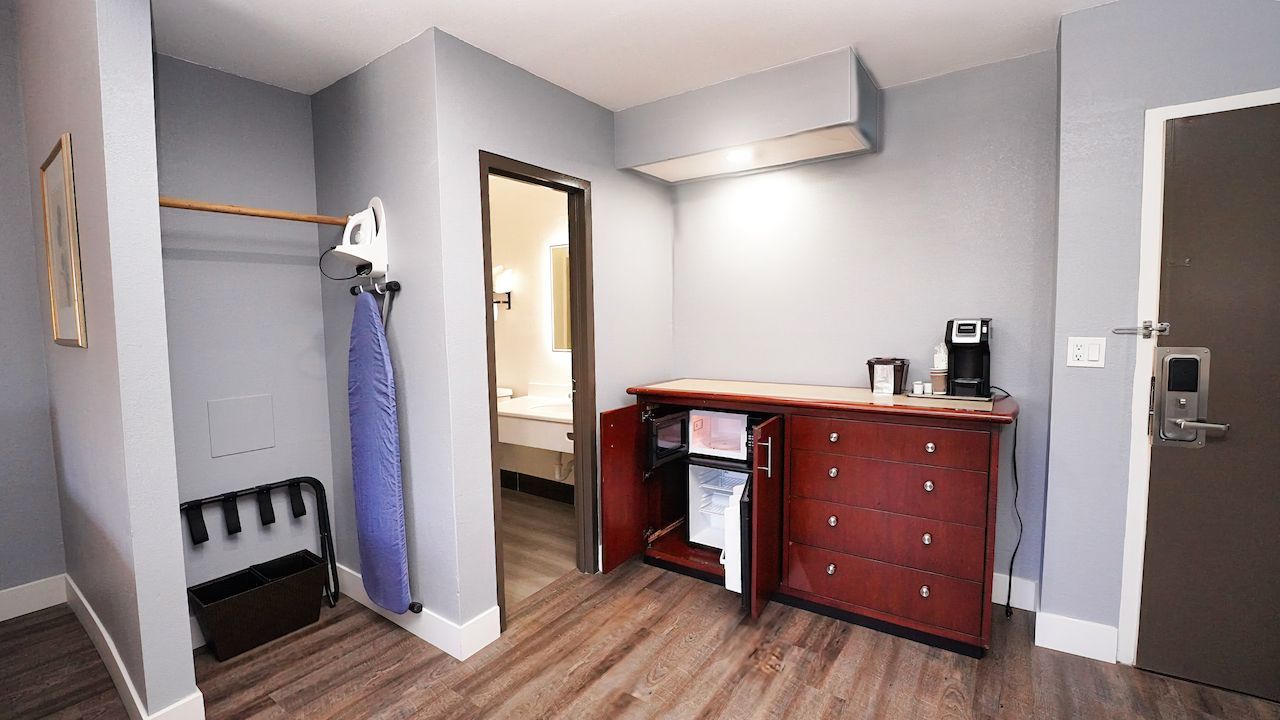 A hotel room with a dresser , ironing board , and coffee maker.