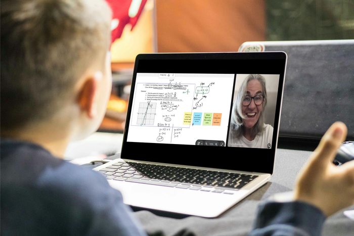 Student making notes looking at a laptop screen showing an excited tutor and work on a shared whiteboard screen