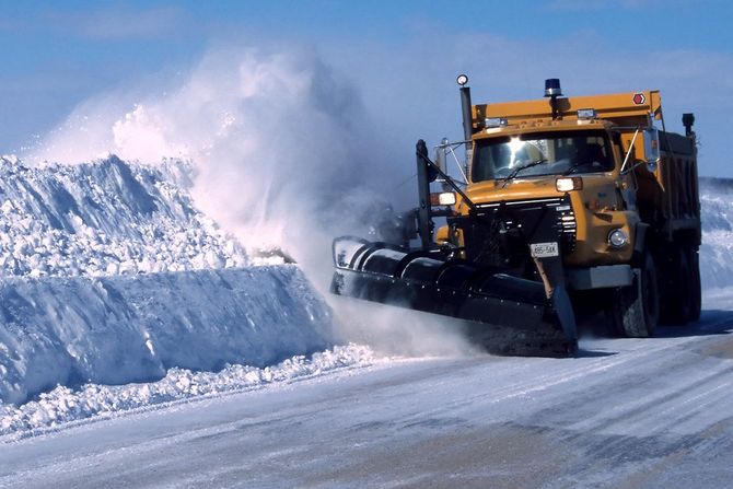 Yellow snowplow clearing a snow-covered road in a winter storm