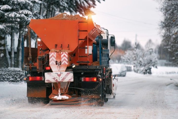 Orange snowplow spreading salt on a snowy road in a winter storm