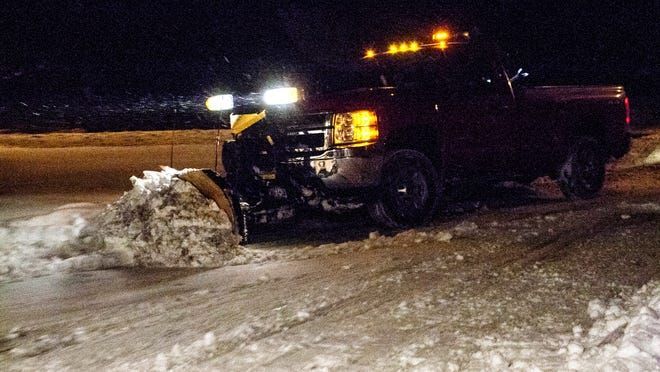Pickup truck with a snow plow clearing snow on a road at night, amber lights flashing