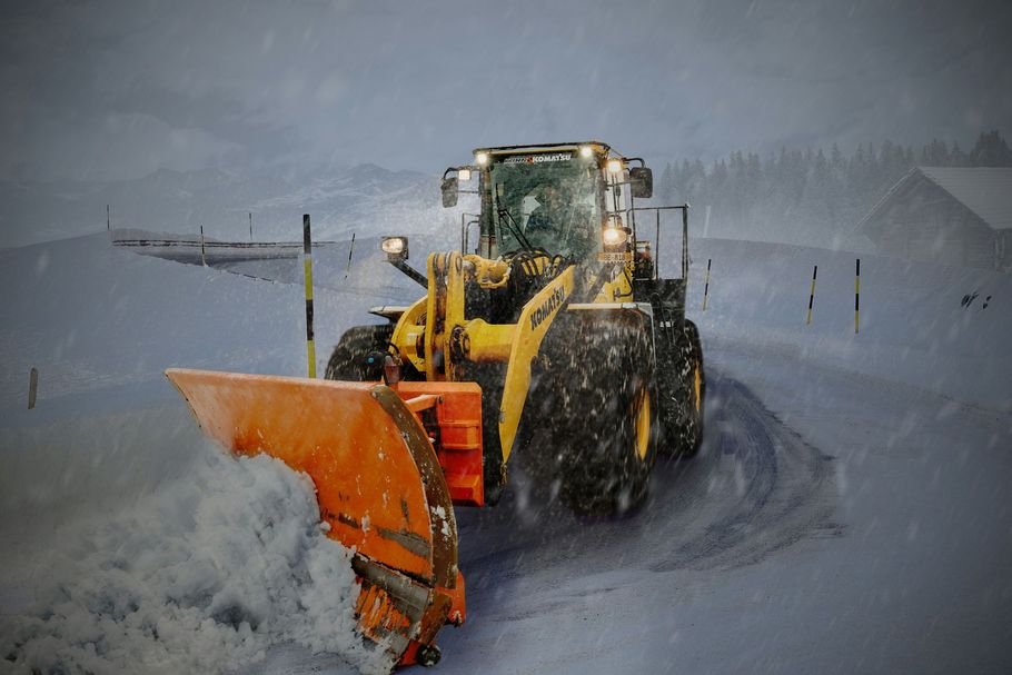 Yellow snowplow clearing a snowy road in a blizzard