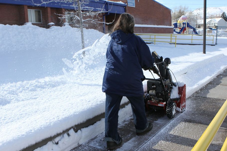 Person clearing snow from a sidewalk with a snowblower beside a snowbank