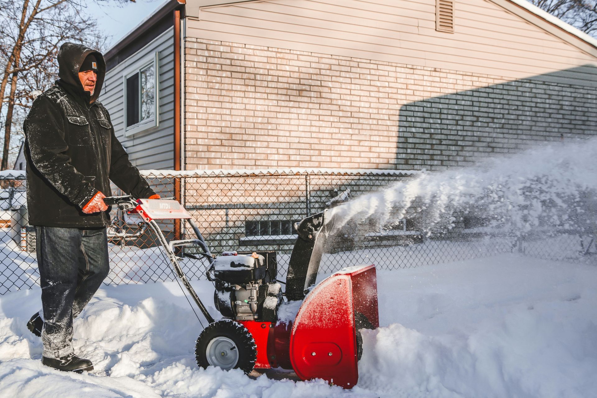 Person using a red snow blower to clear snow outside a house in winter
