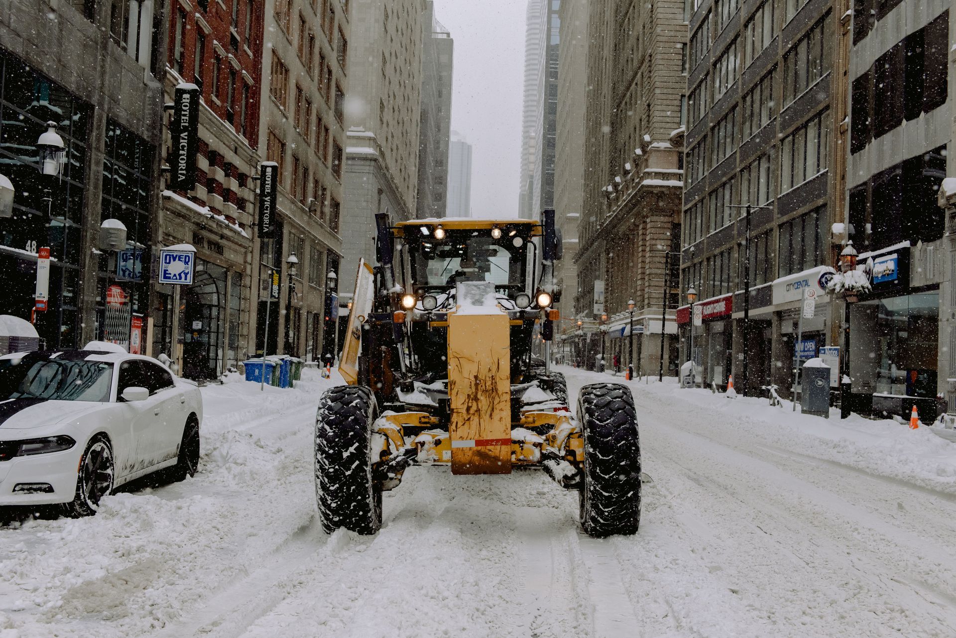 Snowplow clearing a snowy city street between tall buildings