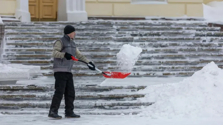 Person shoveling snow on steps in front of a building, with a red snow shovel and large snow piles nearby