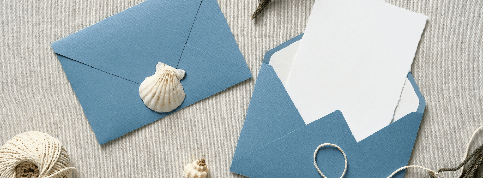A blue envelope with a shell on it and a white piece of paper in it.