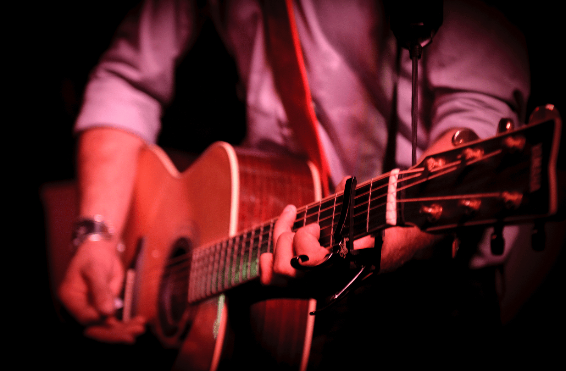 A man is playing an acoustic guitar in front of a microphone.