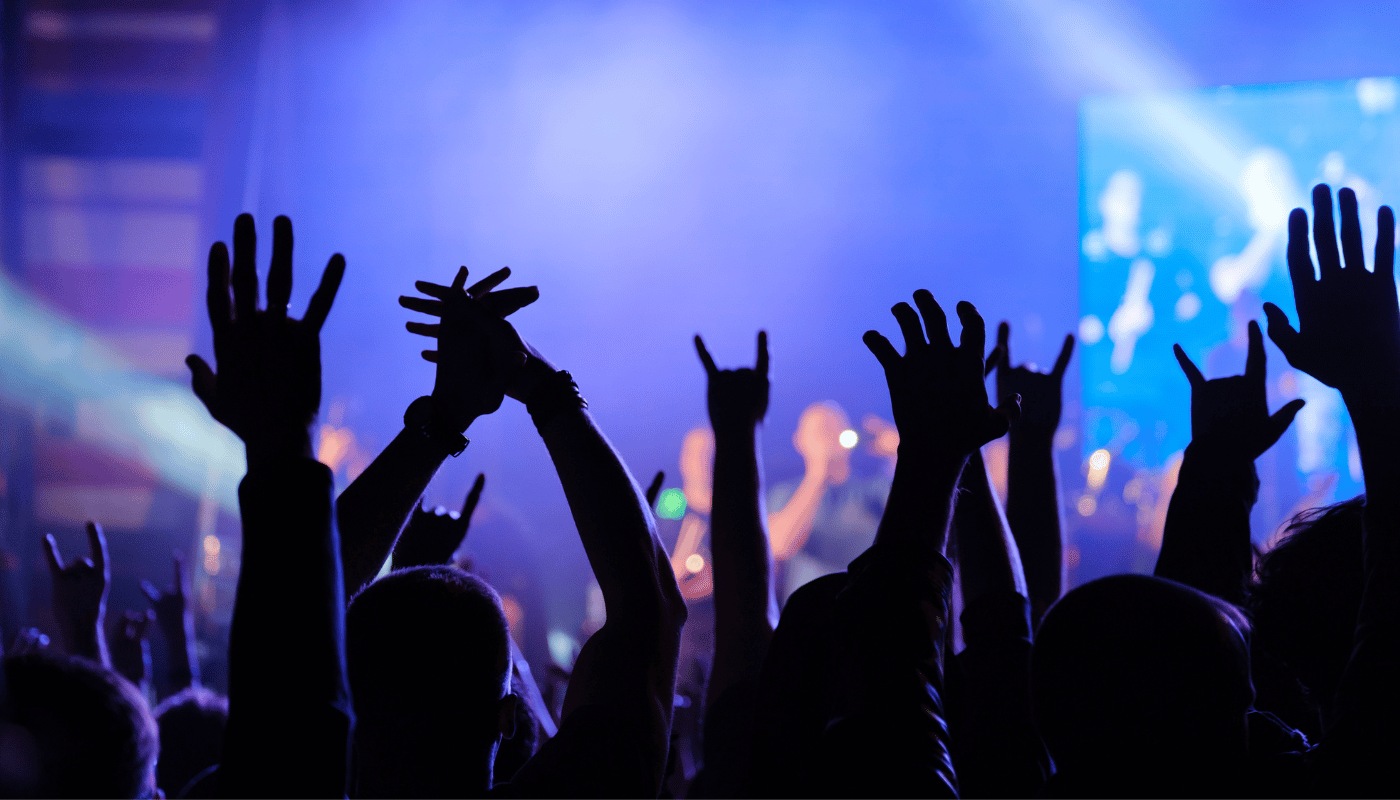 A crowd of people are raising their hands in the air at a concert.