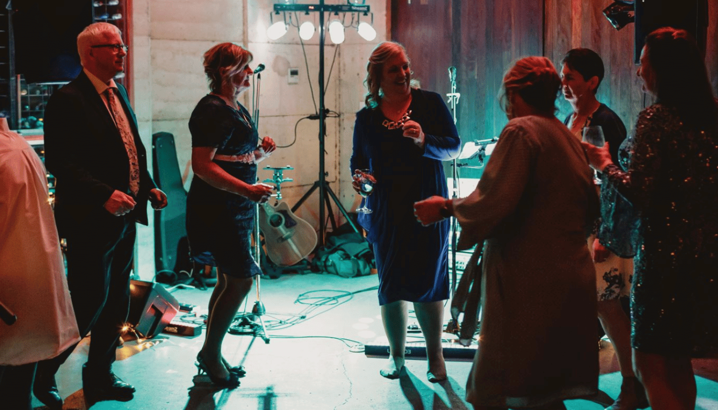 A group of people are dancing in a room with bottles of wine on the wall