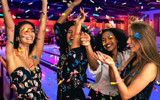 A group of women at fun factory having a party are standing next to each other at a bowling alley and arcade.