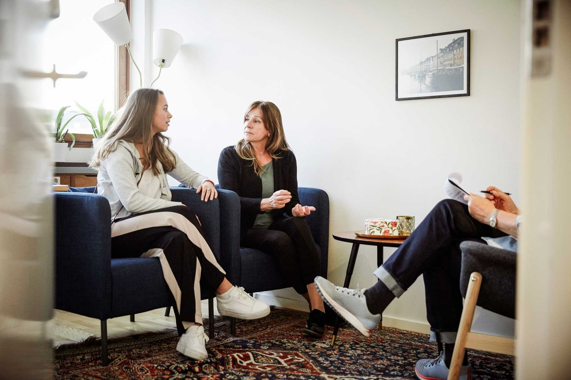A group of people are sitting in chairs in a living room talking to each other.