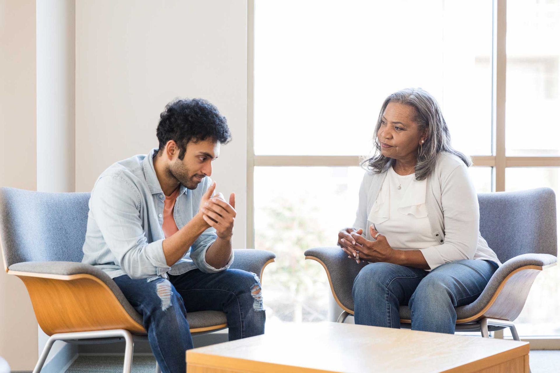 A man and a woman are sitting in chairs talking to each other.