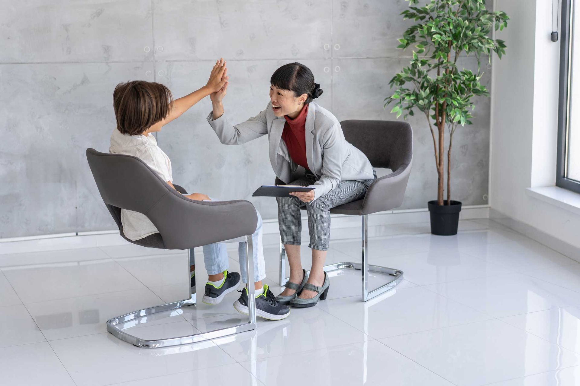 A woman is giving a child a high five while sitting in a chair.