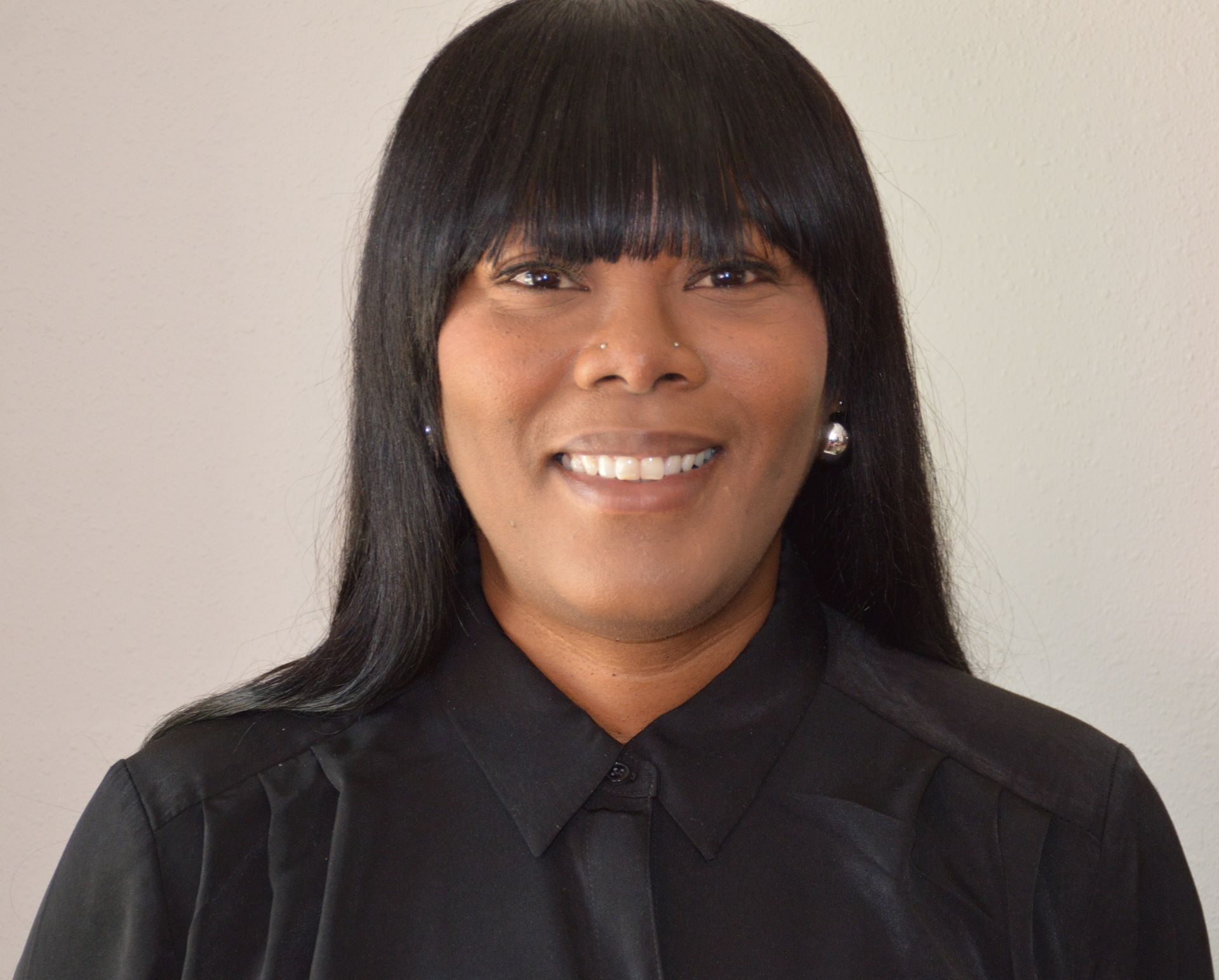 Smiling person in a black shirt and jacket against a plain light background
