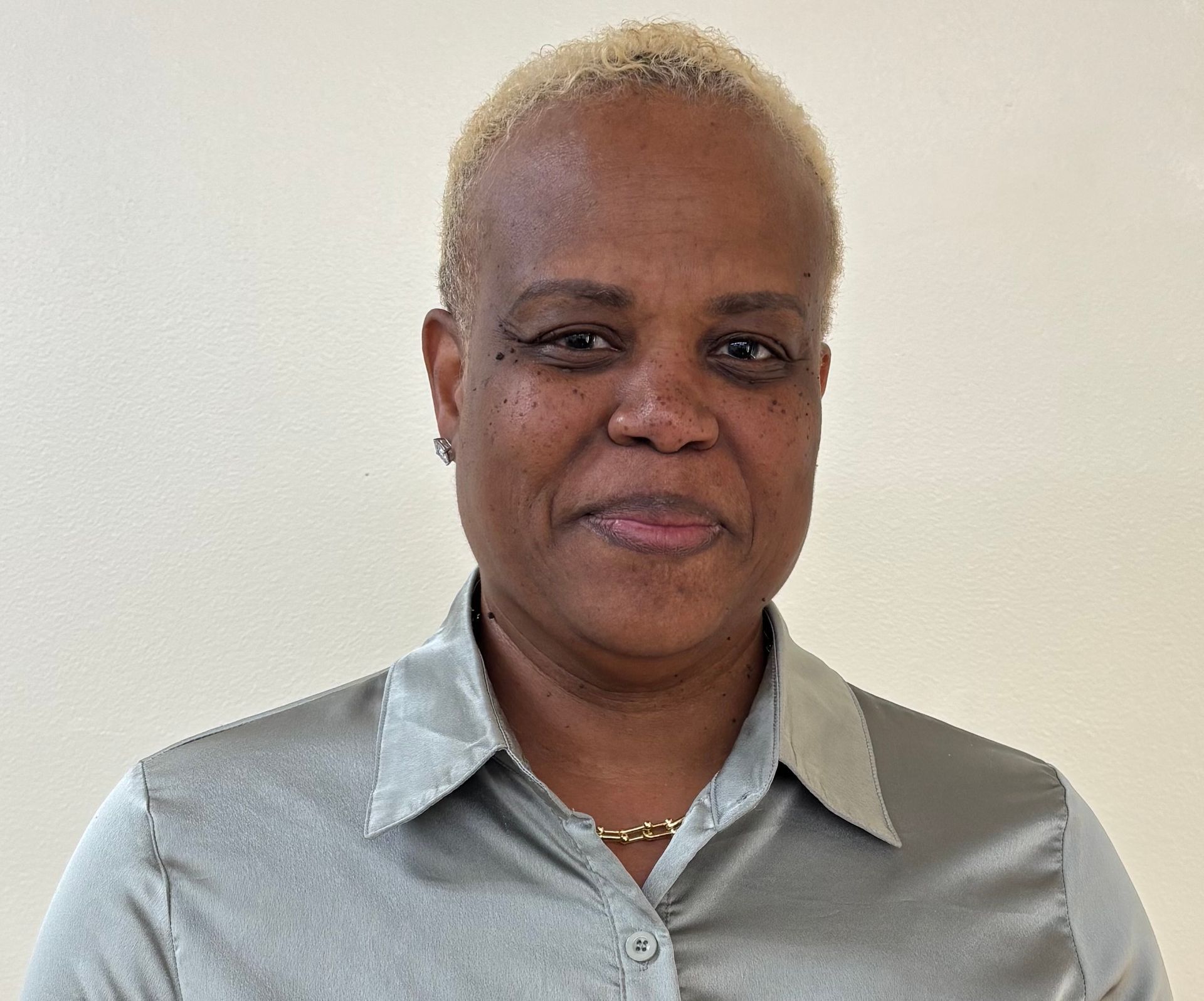 Portrait of a person with short blond hair wearing a light gray collared shirt against a plain wall