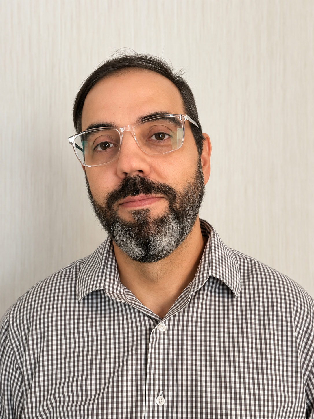 Man wearing glasses and a checkered shirt, facing forward against a plain light background.