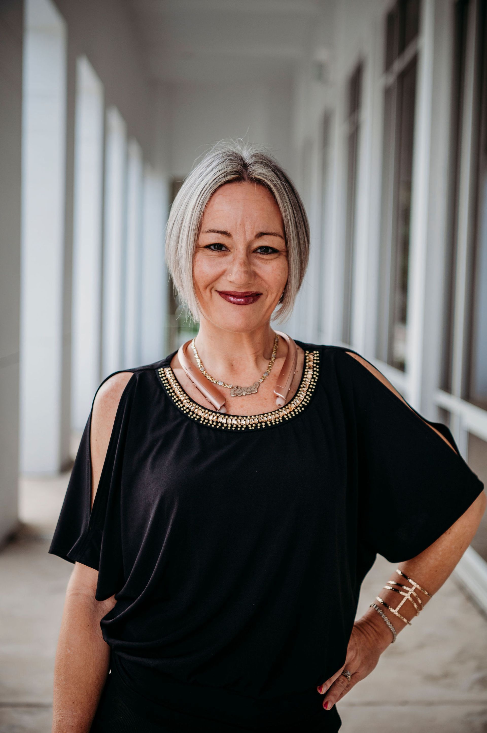 Smiling woman in a black top and gold necklace standing in a bright hallway
