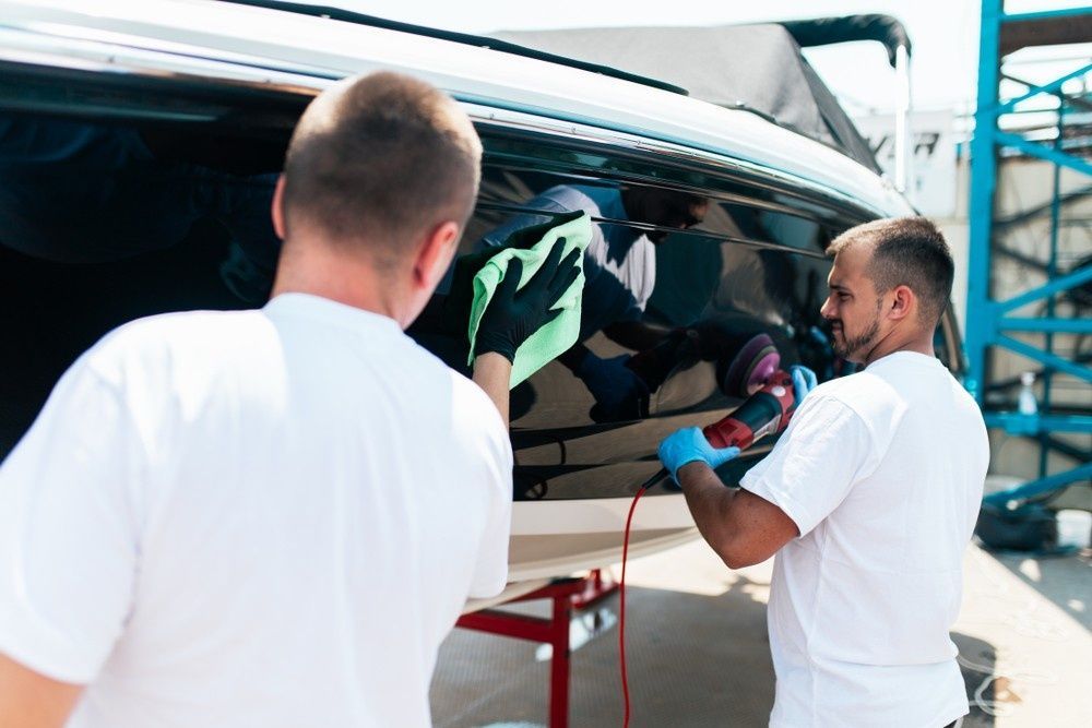 Two People Cleaning a Black Boat Hull; One Uses a Buffer, the Other a Cloth — Ryder's Garage in Erina, NSW