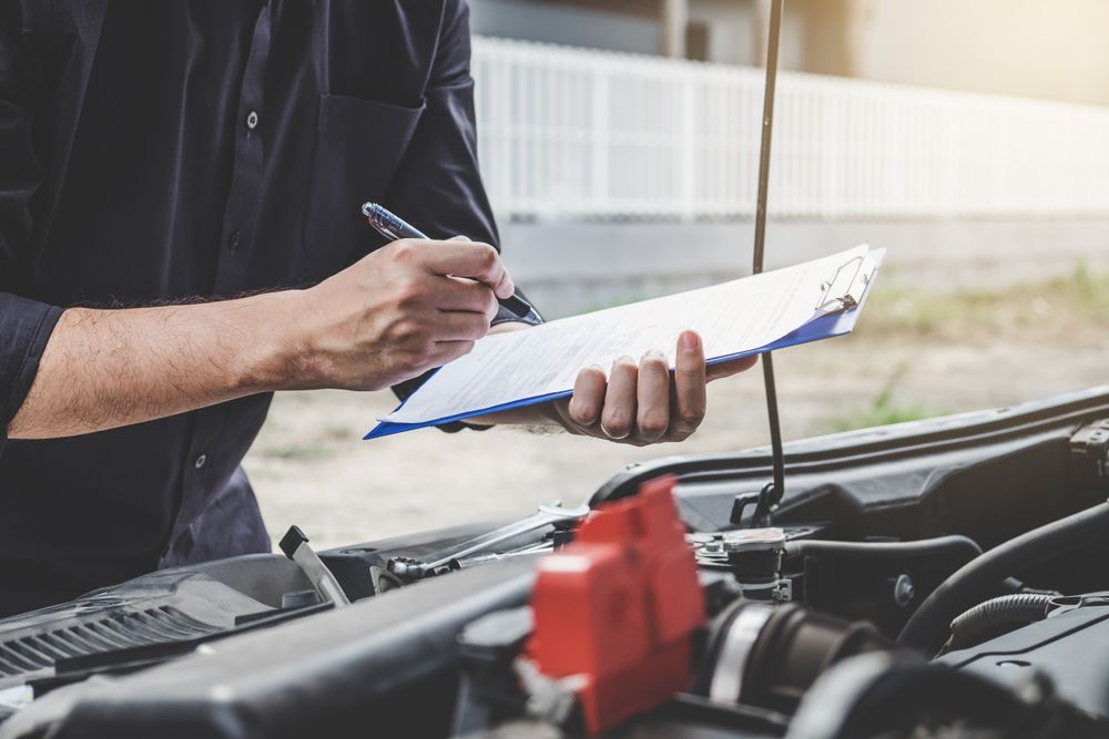 Mechanic Writing on Clipboard While Examining a Car Engine — Ryder's Garage In Kincumber, NSW