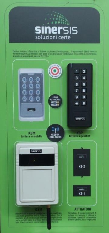Un espositore promozionale verde per i prodotti di sicurezza Sinersis, che mostra tre tastiere e un'unità ricevente per il controllo degli accessi.