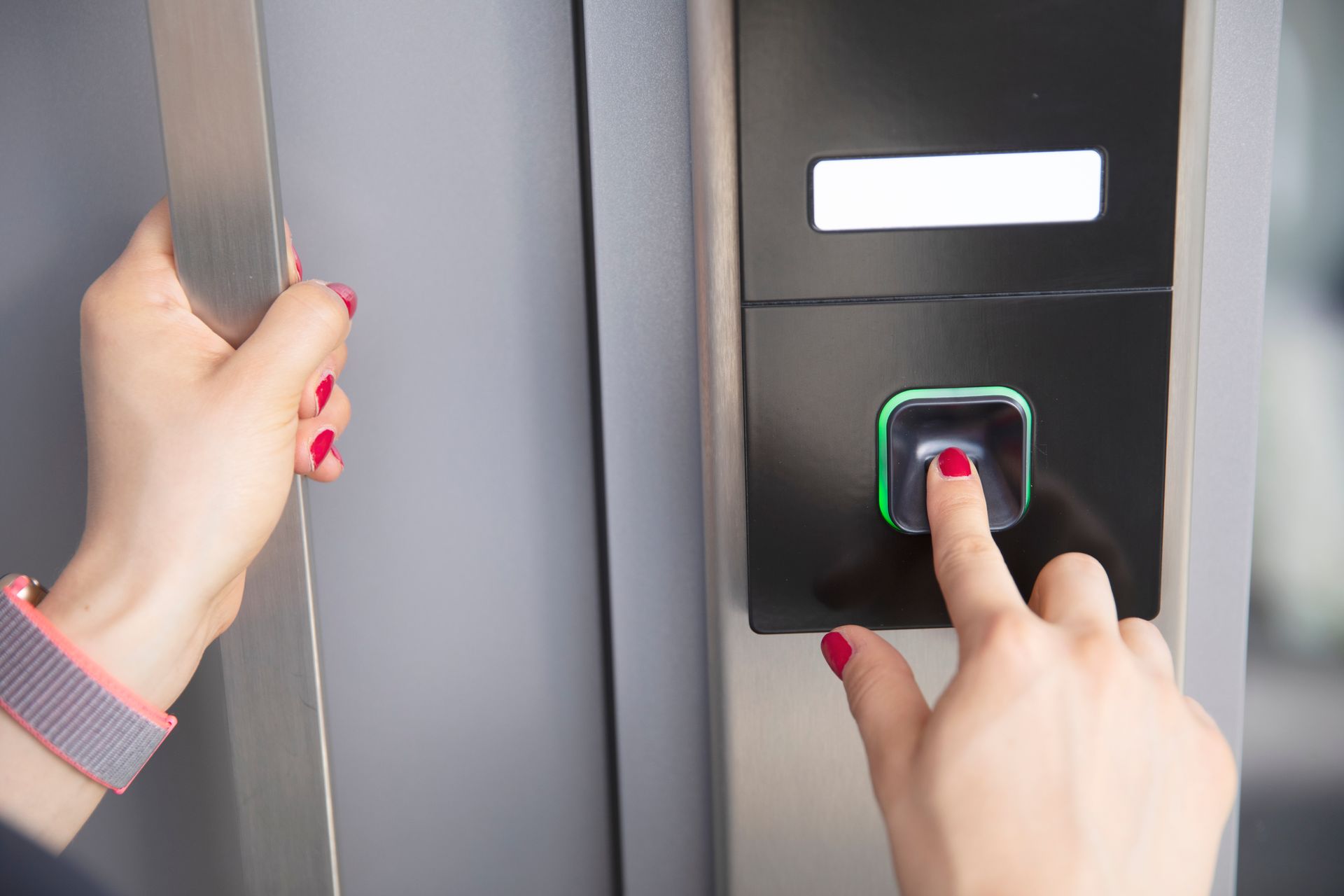 Una persona usa il dito indice per scansionare la propria impronta digitale su una serratura biometrica elettronica nera posta sullo stipite di una porta.
