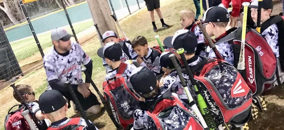 Cyclists in black and red jerseys gathered around a coach on a dirt track